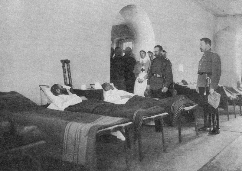Посещение Императором Николаем II города Ровно. Император Николай II с сестрой, вел. княгиней Ольгой Александровной, обходят раненых во время посещения госпиталя Евгеньевской общины Красного Креста имени вел. княгини Ольги Александровны, в котором вел. княгиня с начала войны работает рядовой лазаретной сестрой милосердия. Присутствует дворцовый комендант генерал-майор свиты В.Н.Воейков (в проеме арки слева) и др. 26.01.1915. г. Ровно.